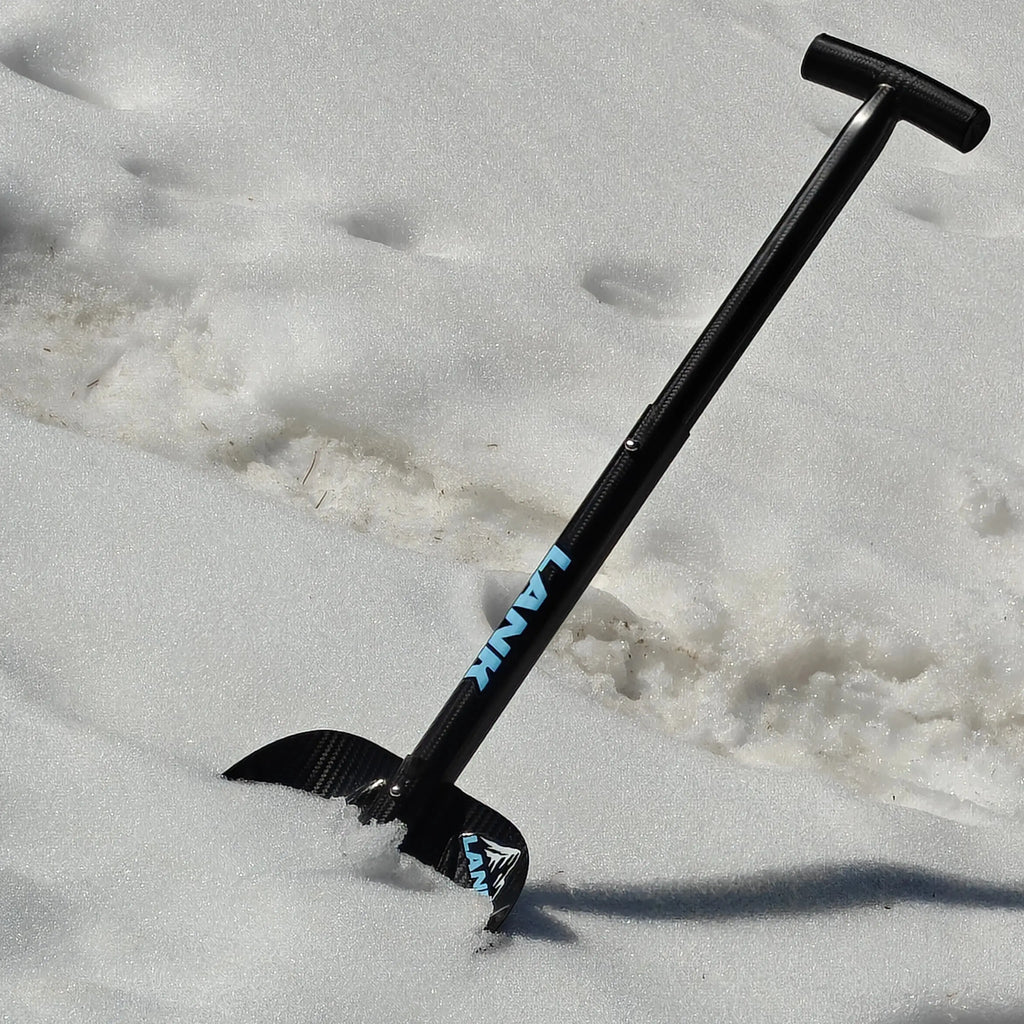 Lightweight carbon fiber avalanche shovel with a telescopic handle, partially resting in deep snow on a mountain slope.
