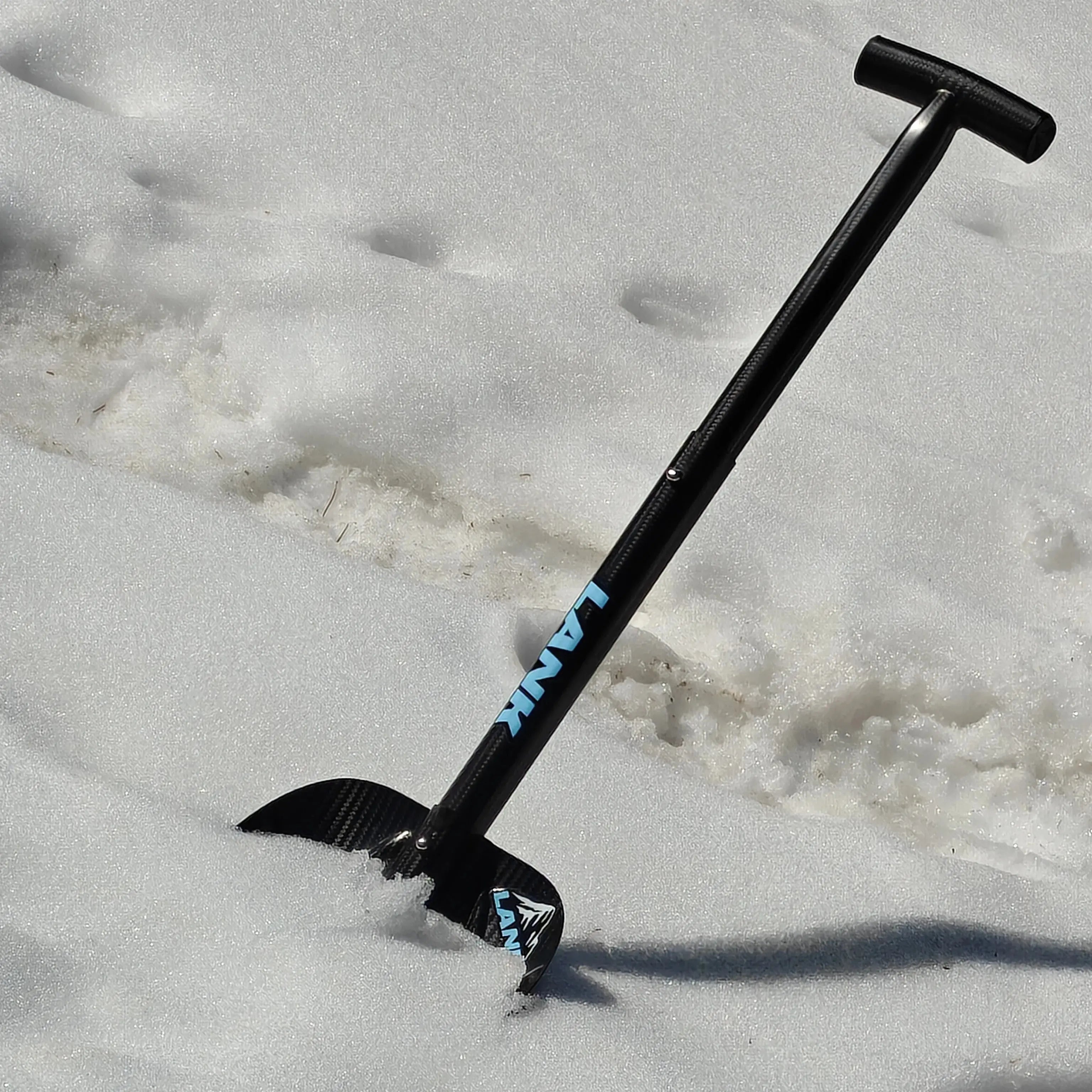 Lightweight carbon fiber avalanche shovel with a telescopic handle, partially resting in deep snow on a mountain slope.