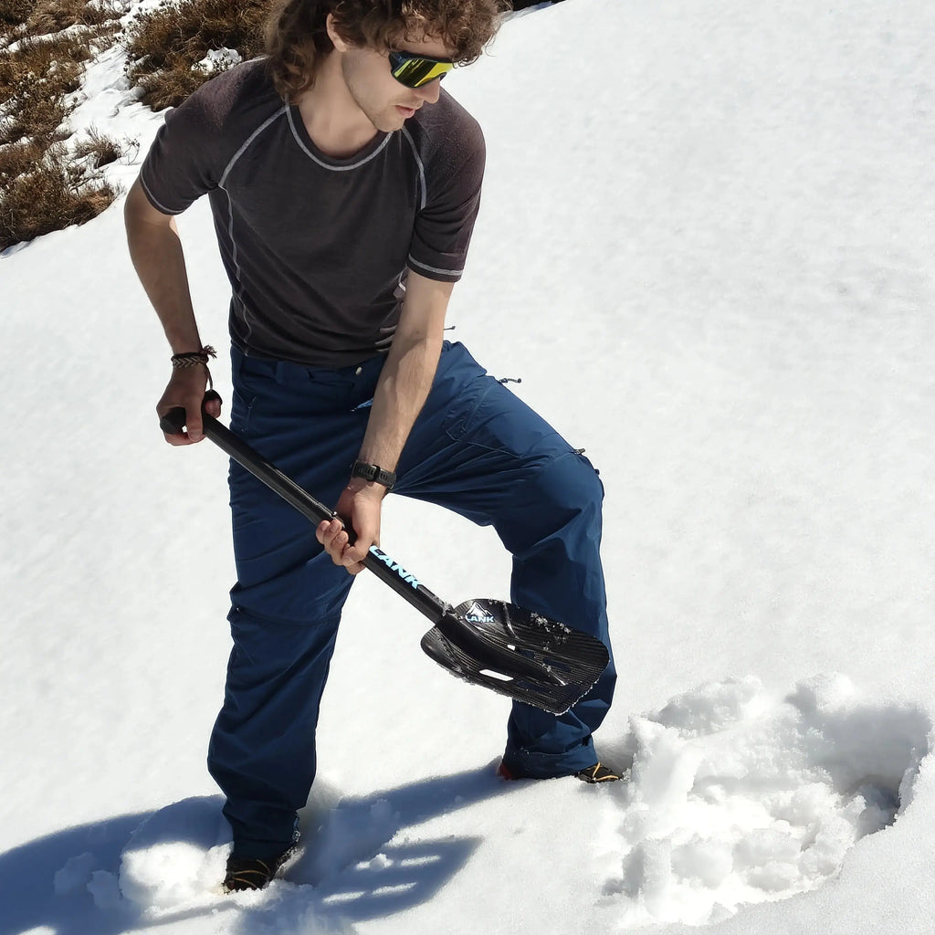 Shoveling snow in the mountains with a lightweight carbon fiber avalanche shovel featuring an extended telescopic shaft.
