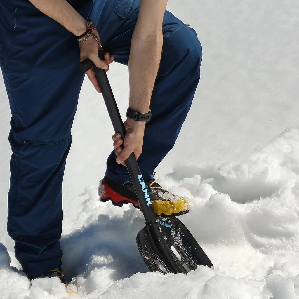 Person shoveling snow with a carbon fiber avalanche shovel in the mountains prone to avalanches.